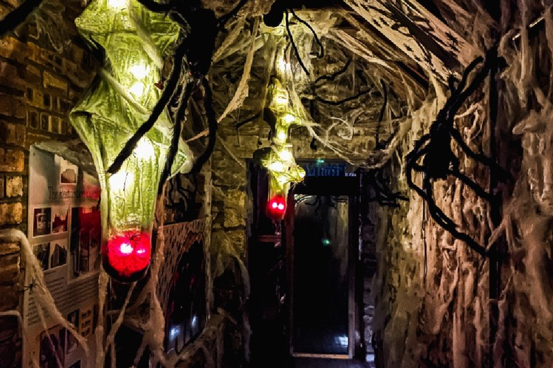 two green Halloween lanterns hanging from ceiling with red lights inside. There is a fake big spider on the wall
