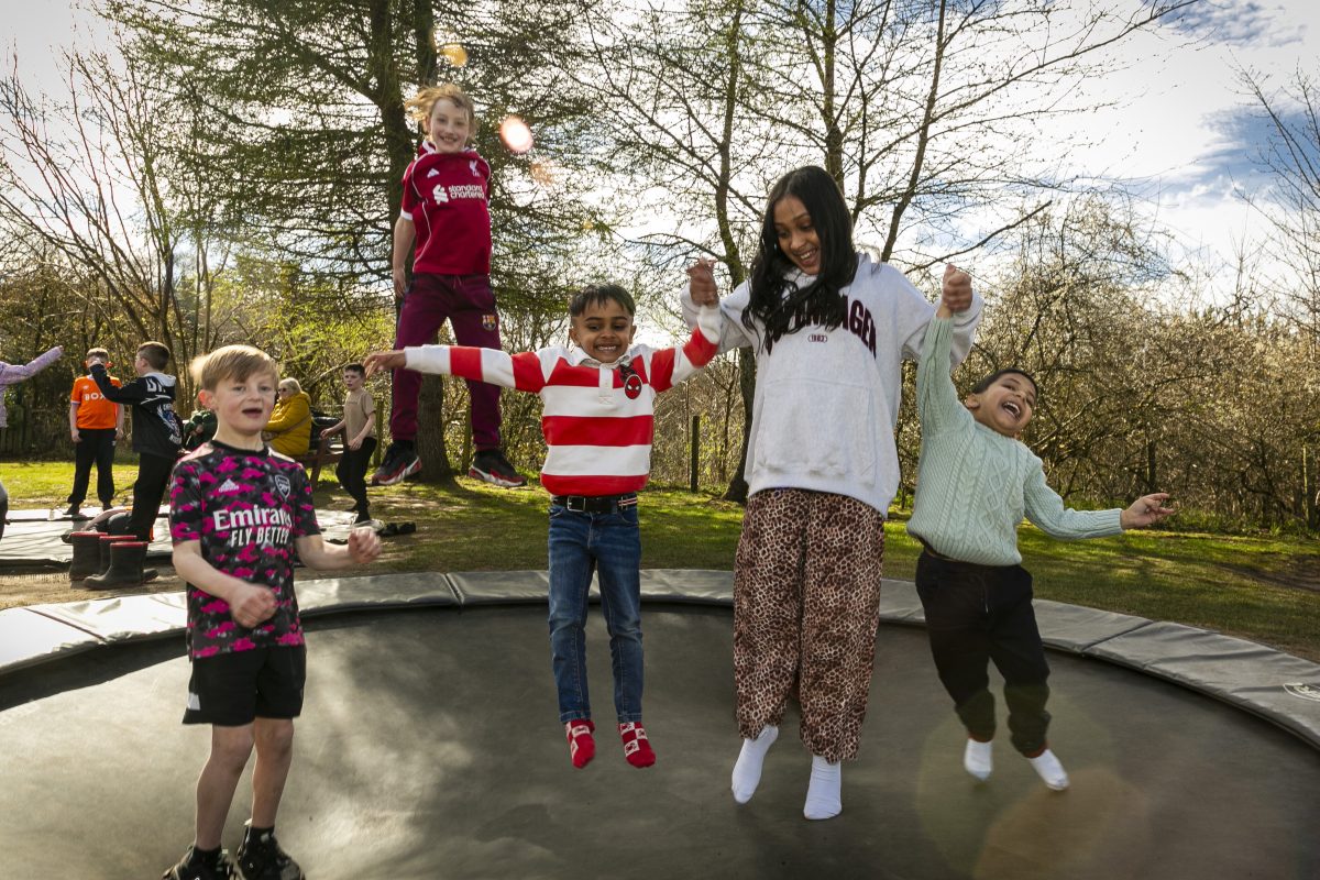 A group of five children play on an outdoor trampoline. They are all laughing.
