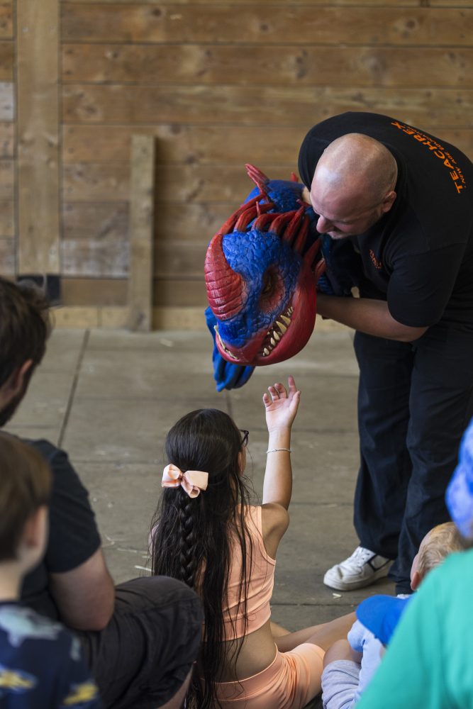 A small blue and red dragon puppet leans towards a child who reaches up to touch them.