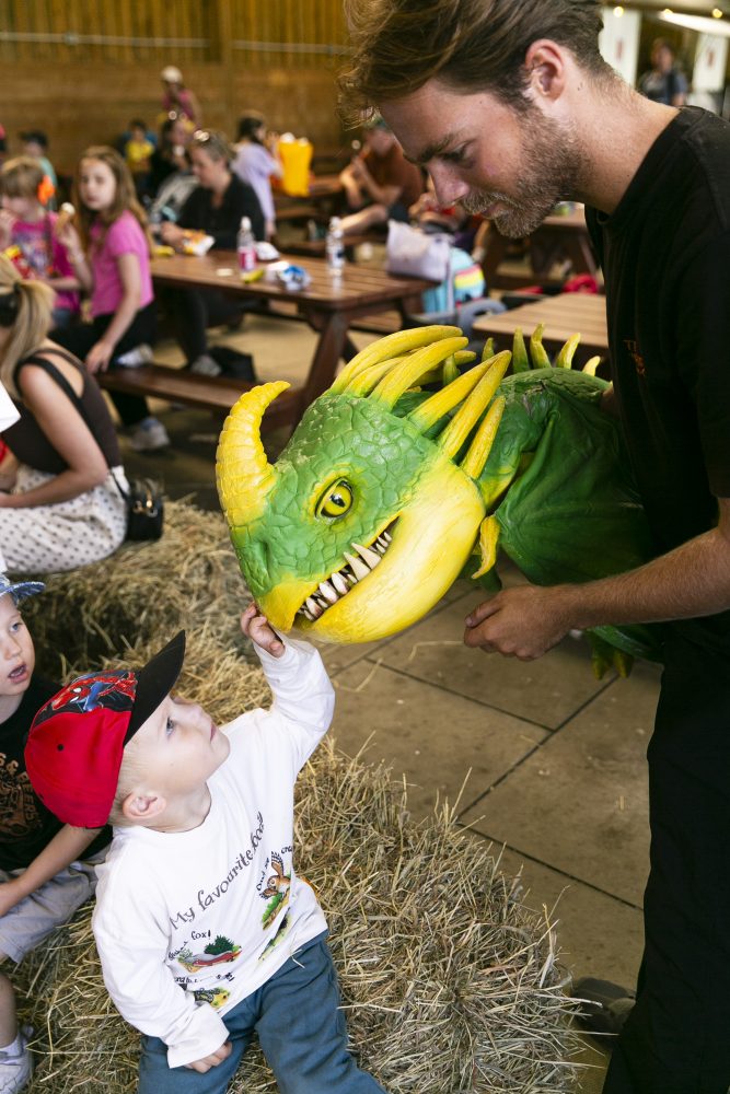 A yellow and green dragon puppet reaches down towards a young child.
