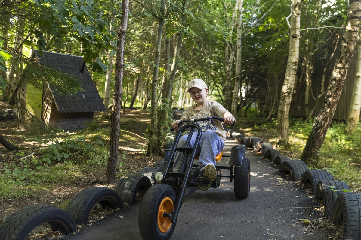 A twelve year old boy is on a go kart with a forest in the background.